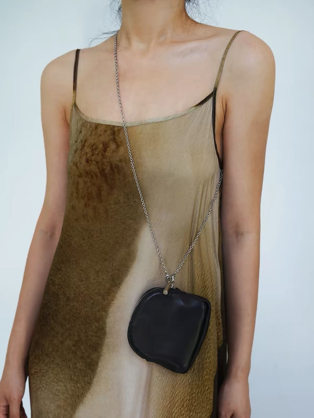 A model wearing a brown and beige animal-print camisole dress, accessorized with a silver chain crossbody bag holding a black pouch.