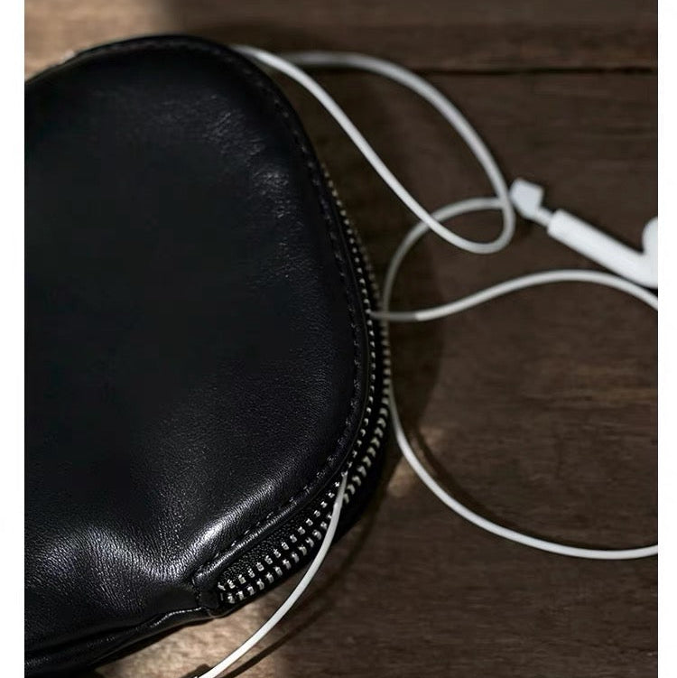 A close-up of a black zippered pouch or case on a dark wooden surface, with white wired earphones partially visible and draped across it. 