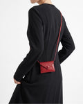 A model wearing a black long-sleeve dress is shown from the back, wearing a small red envelope-style crossbody bag with a thin red strap.