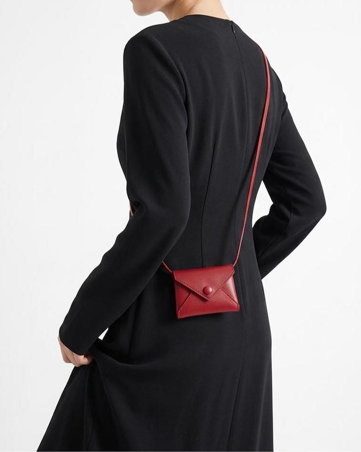 A model wearing a black long-sleeve dress is shown from the back, wearing a small red envelope-style crossbody bag with a thin red strap.